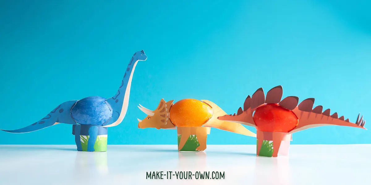 Three dinosaurs made from painted plastic eggs against a blue background